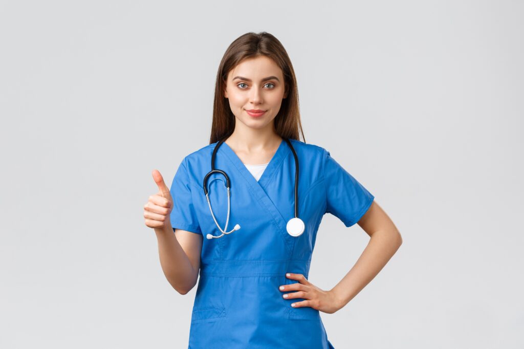 Medical workers, covid-19 and vaccination concept. Confident professional doctor, female nurse in blue scrubs and stethoscope, show thumbs-up, assure or guarantee best quality of service in clinic